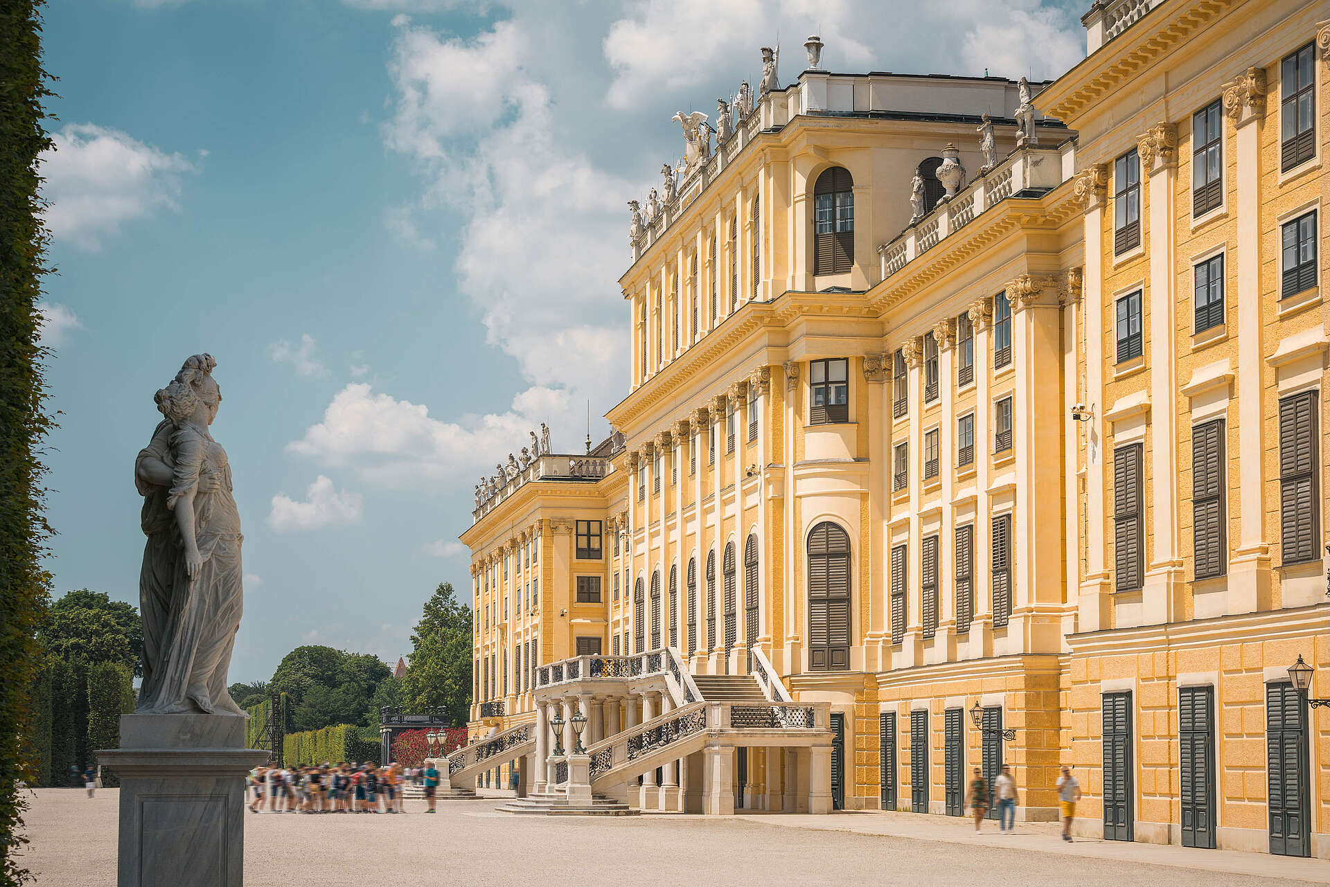 Seitlicher Blick auf Schloss Schönbrunn mit Statue links und Touristengruppe im Hintergrund