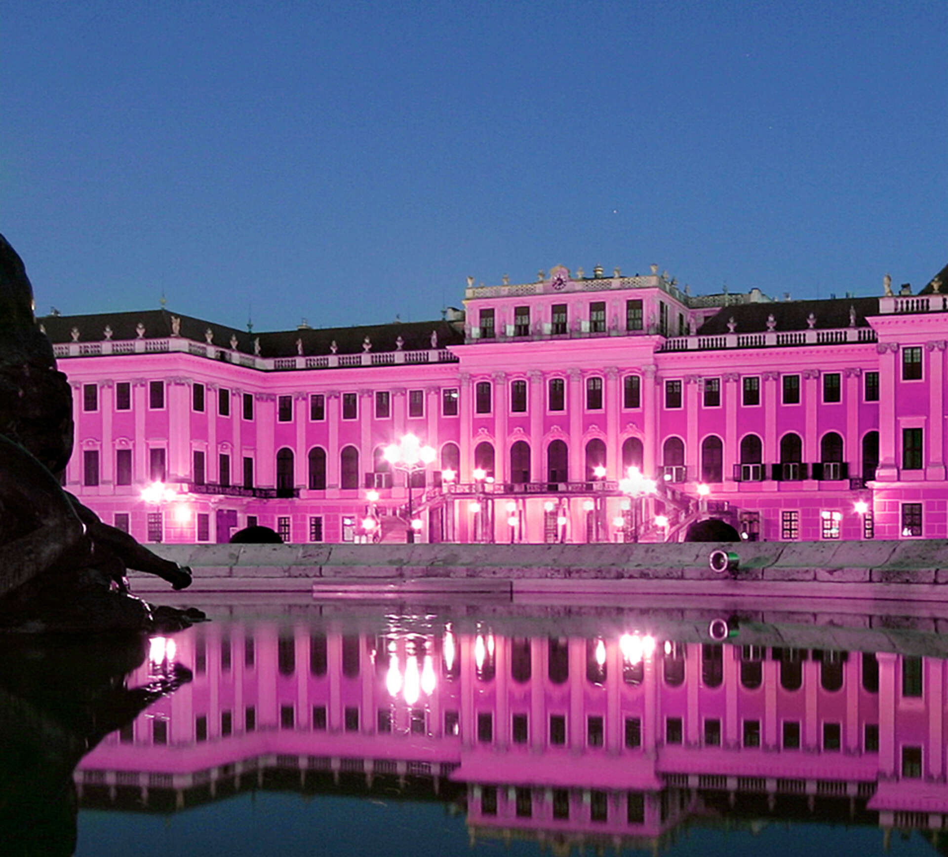 Schönbrunn Palace illuminated in pink, the palace reflected in the fountain